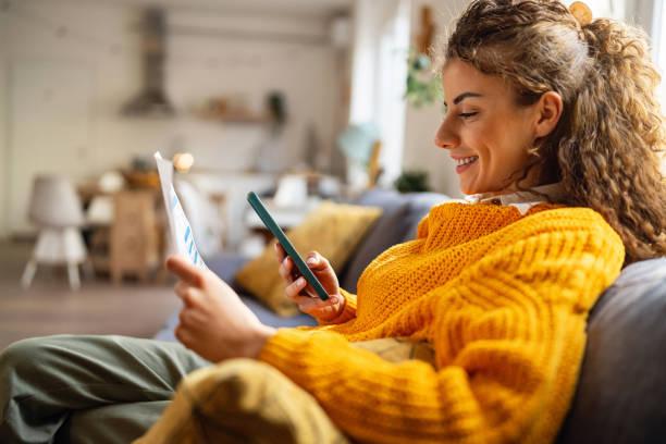 Young woman using e-banking to pay bills from home Side-view of an young Caucasian woman using smartphone for scanning the QR code and paying the bill Debt management stock pictures, royalty-free photos & images